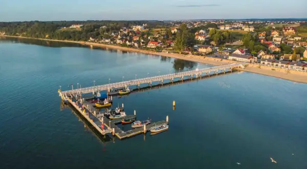 Molo w Mechelinkach z łodziami i widokiem na plażę i zabudowania. To świetne mechelinki atrakcje dla każdego.