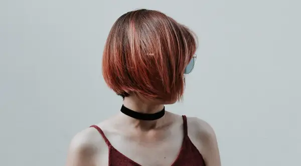 Kobieta z rudymi, krótkimi włosami i okularami przeciwsłonecznymi. Stylowy, krótki bob to świetny pomysł na styling włosów krótkich.