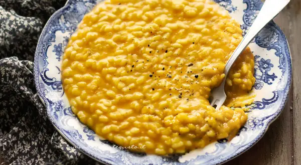 Un cremoso risotto alla zucca, servito su un piatto decorato, con una forchetta che affonda nel piatto.