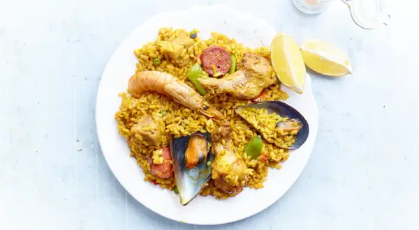 Une assiette de paella royale, garnie de crevettes, moules, poulet, chorizo et riz jaune, avec des quartiers de citron.