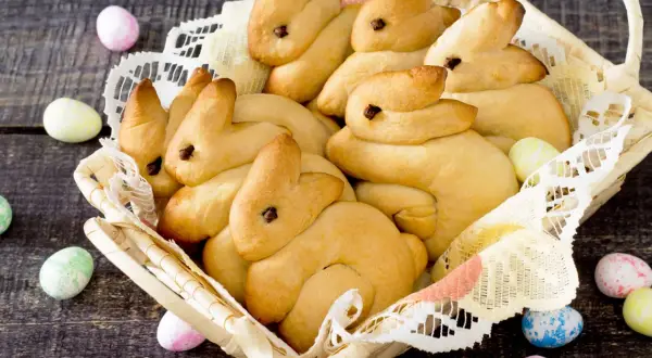 Korb voller goldbrauner Quark Osterhasen, umgeben von bunten Ostereiern auf dunklem Holz.