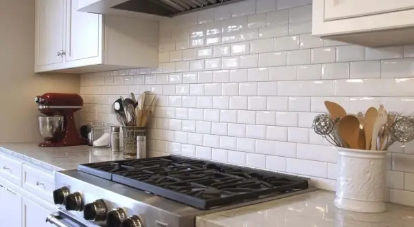 A clean kitchen backsplash installation with white subway tiles, a red stand mixer, and cooking utensils.
