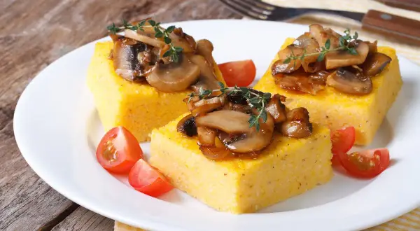 Trzy kwadratowe porcje polenty, podane z duszonymi pieczarkami i pomidorkami koktajlowymi. Pyszne danie, które pokazuje, co to polenta.