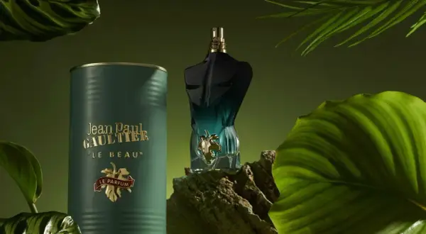 Flakon perfum Jean Paul Gaultier Le Beau Le Parfum w otoczeniu zielonych liści i mchu.