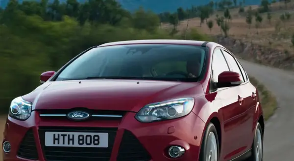 Czerwony Ford Focus 2011 na krętej drodze wśród zieleni.