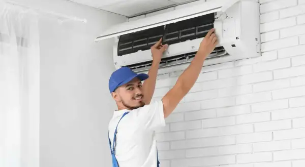 Tecnico con cappellino blu esegue la sanificazione aria condizionata, controllando i filtri per un'aria più pulita.