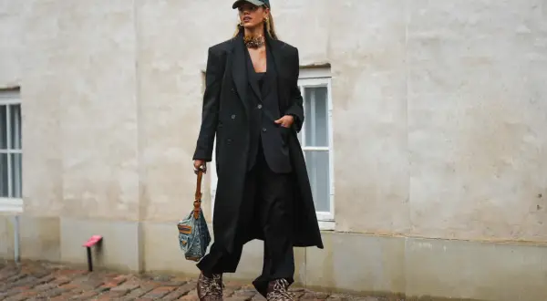Elegancka stylizacja z czapką z daszkiem. Kobieta w czarnym garniturze i płaszczu, z torebką i modną czapką.