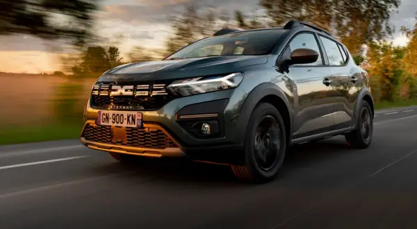 Zielony Dacia Sandero Stepway pędzi po drodze o zachodzie słońca, otoczony rozmazanymi drzewami i mglistym krajobrazem.