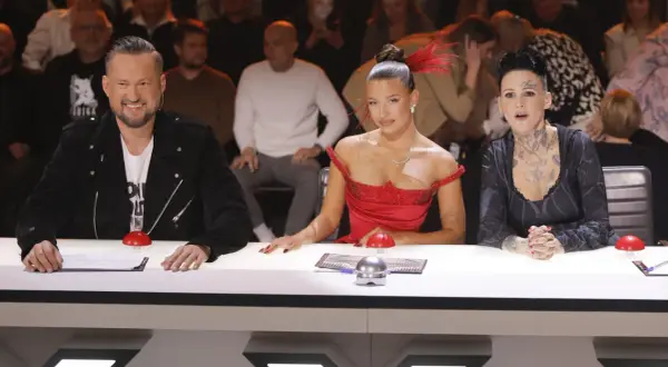 Trzy osoby siedzące przy stole jurorskim, w tym dwie kobiety w sukniach i mężczyzna w czarnej kurtce.