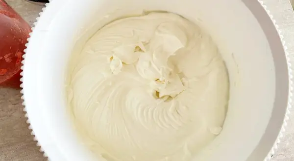 Gładka, kremowa masa z mascarpone w białej misie, gotowa do deseru. Obok widać miseczkę z truskawkami.