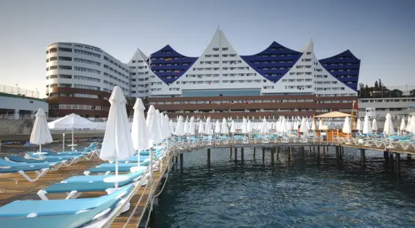 Widok na Orange County Resort Alanya z pomostem pełnym leżaków i parasoli, z błękitnym morzem w tle.