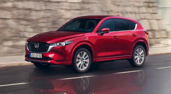 Czerwony suv Mazda CX-5 jedzie po mokrej drodze, odbijając się w kałuży.