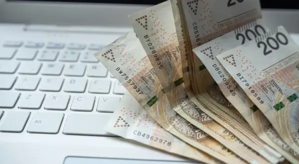 Banknoty 200 zł leżące na białej klawiaturze laptopa.