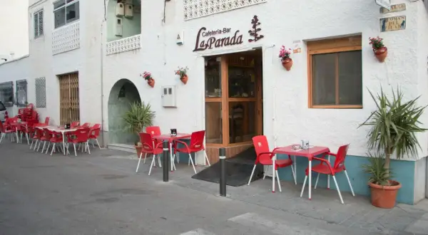 Cafetería-Bar "La Parada", un lugar acogedor donde comer en Níjar. Mesas rojas y sillas esperan en la acera.