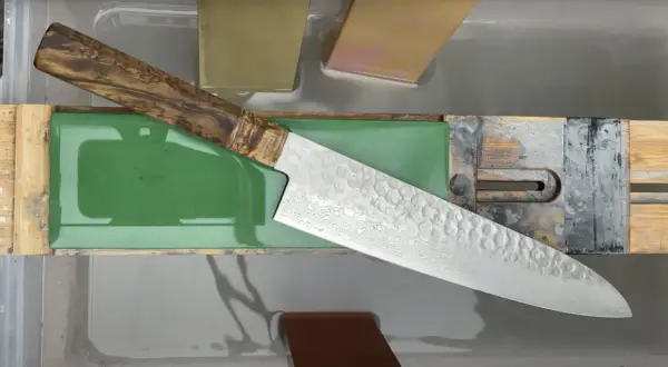 Ein japanisches Messer mit Damastmuster wird auf einem Schleifstein mit präzisem Schleifwinkel geschärft.