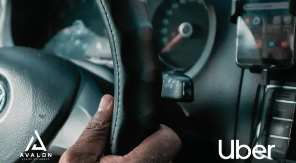 Dłoń kierowcy na kierownicy, obok smartfon z aplikacją Uber.