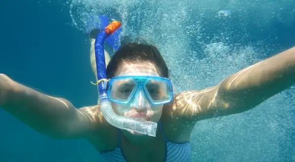 Dziewczyna w masce i rurce do oddychania pływa pod wodą. To właśnie snorkeling – odkrywanie podwodnego świata!