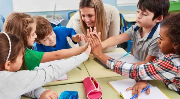 Niños y maestra celebran con un choque de manos, fomentando la motivación en el aula.