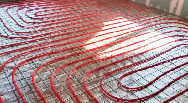 Czerwone rury ogrzewania podłogowego ułożone na siatce na podłodze w trakcie budowy.