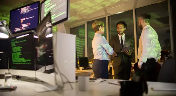 Zespół omawia strategię cyberbezpieczeństwa firmy przy monitorach z kodem.
