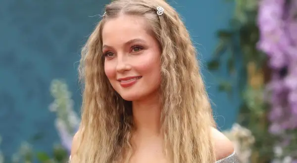 Hannah Dodd, con cabello rubio ondulado y adornos florales, sonríe con un vestido plateado.