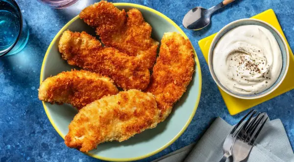 En tallrik med gyllene, krispig kyckling som ser utsökt ut. Bredvid finns en skål med krämig dipp och bestick.