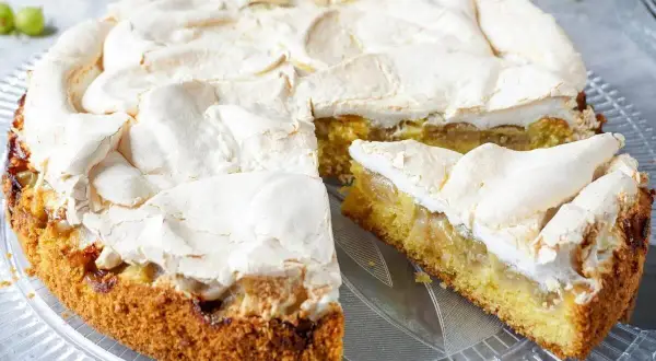 Ein saftiger Stachelbeer Baiser Kuchen mit goldbraunem Boden und fluffiger Baiserhaube, ein Stück ist angeschnitten.