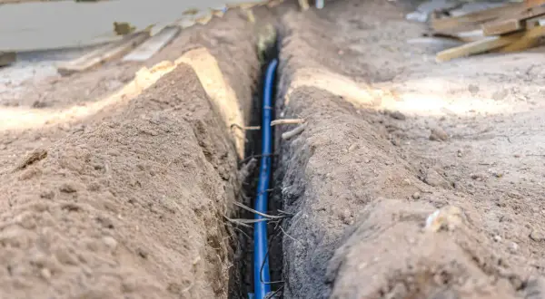 Wykonanie instalacji elektrycznej w ziemi wymaga przestrzegania przepisów. W wykopie widoczny jest niebieski kabel.