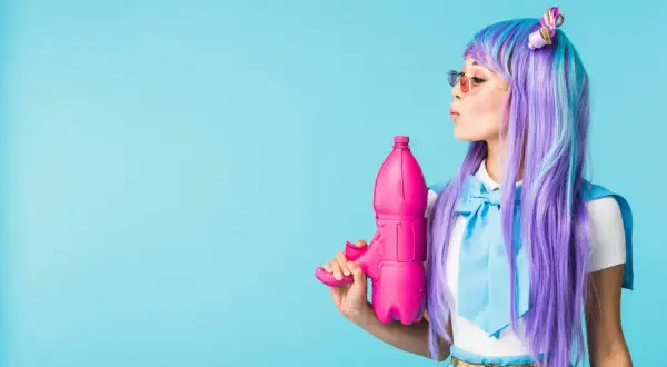 Dziewczyna w peruce w stylu kawaii z fioletowymi i niebieskimi włosami trzyma różowy pistolet na wodę.