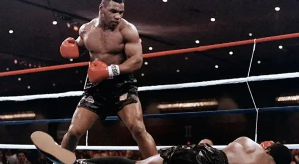 Mike Tyson, in his iconic boxing stance, stands over a fallen opponent. This image captures the intensity of a Mike Tyson workout, showcasing his power and dominance in the ring.