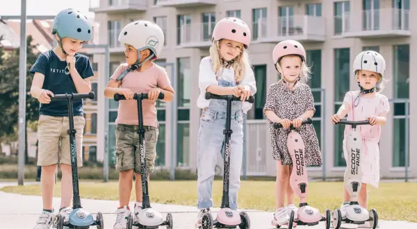 Fizjoterapeuta poleca Scoot and Ride dla dzieci. Pięcioro maluchów w kaskach na hulajnogach, gotowych do zabawy.