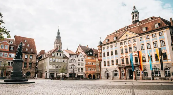 Blick über den Marktplatz der Coburg Altstadt mit historischen Gebäuden, einem Denkmal und Fahnen.