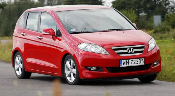 Czerwona Honda FR-V jedzie po drodze, otoczona zielenią.