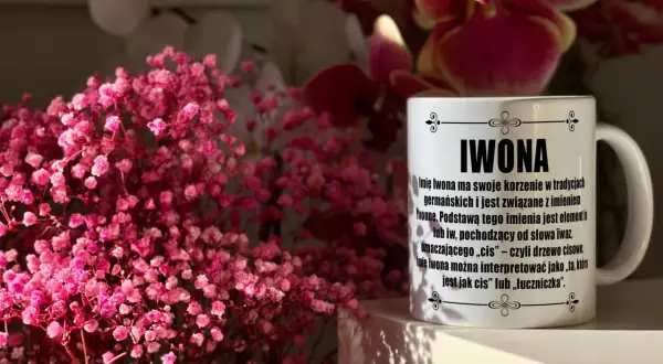 Biały kubek z napisem "IWONA" na tle różowych kwiatów i orchidei.