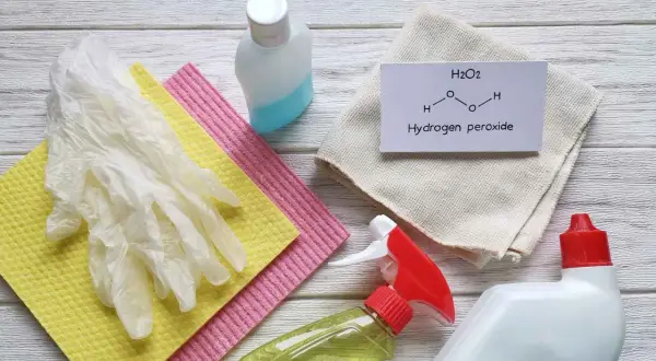 Guanti, panni e flaconi per la pulizia, con un foglietto che spiega che cos'è il perossido di idrogeno (H2O2).