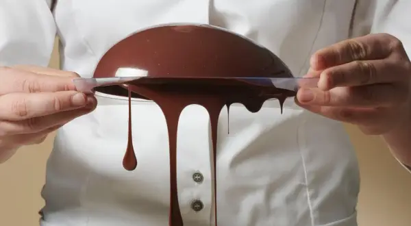 Comment faire du chocolat au lait : une demi-sphère de chocolat coule d'un moule transparent tenu par des mains.