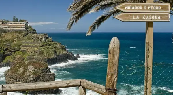 Cartel indicador en el sendero rambla de castro, señalizando Mirador S. Pedro y La Casona, con el mar azul de fondo.
