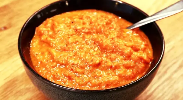 En skål med krämig ajvar, perfekt för ditt ajvar recept. En sked vilar i den orangea röra.