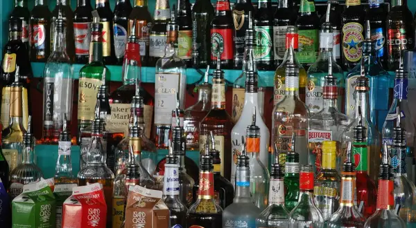 Różnorodne butelki alkoholi, od whisky po rum, stoją na półce. Zastanawiasz się, jak obliczyć procent nalewki?
