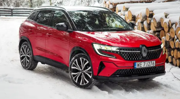 Czerwony Renault Austral na śniegu, z widocznymi felgami i grillem. Poznaj jego wymiary i możliwości w zimowych warunkach.
