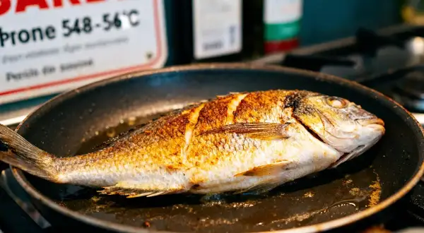 Poisson entier doré dans une poêle, prêt pour une recette gastronomique facile.