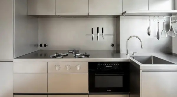 Cucina moderna con piano cottura a gas, forno, lavello e utensili appesi, tutto in lucido acciaio inox 18/10.