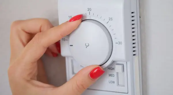 Mano ajustando el termostato para saber como poner la calefacción en casa. La temperatura se marca en grados Celsius.
