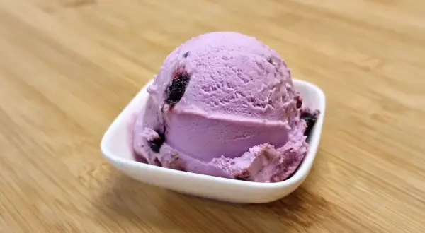 Ein Löffel Amarena-Eis mit Fruchtstückchen, das leicht nach Alkohol duftet, in einer weißen Schale auf Holzuntergrund.