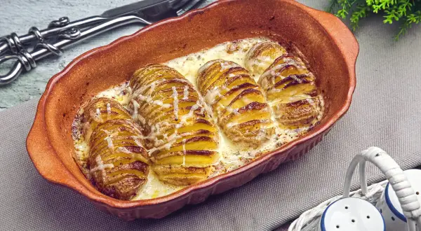 Gerichte mit Kartoffeln: Hasselback-Kartoffeln in cremiger Sauce, goldbraun gebacken und mit Käse überbacken, serviert in einer Terrine.