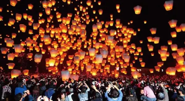 Tysiące lampionów unosi się na nocnym niebie, tworząc magiczny widok podczas święta lampionów. Tłum ludzi obserwuje to widowisko.
