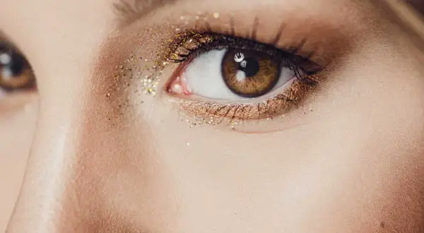 Un œil marron orné d'un maquillage soirée doré scintillant, parfait pour briller toute la nuit.