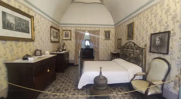 Camera da letto nella casa di d'Annunzio, con carta da parati floreale, letto in ferro battuto e mobili d'epoca.