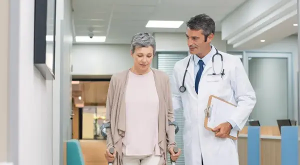 Lekarz wspiera pacjentkę po urazie, która porusza się o kulach. Postęp w leczeniu traumatologii jest widoczny.