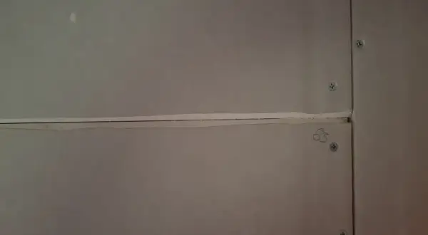 Närbild på gipsskivor där skarvarna spacklas för att skapa en jämn yta. Skruvarna syns tydligt.